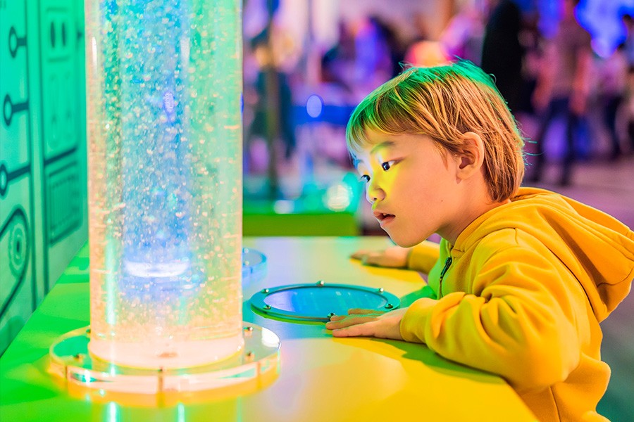 A young boy mesmerized by a vibrant light display at a Children's Museum, filled with wonder and excitement