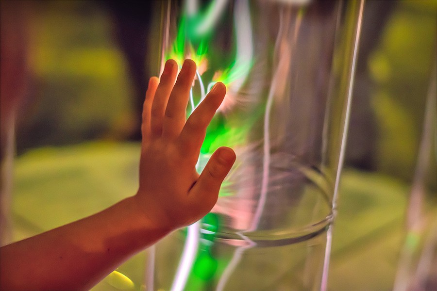 A child's hand reaching into a glowing green tube at Children's Museums in Singapore, exploring light and discovery