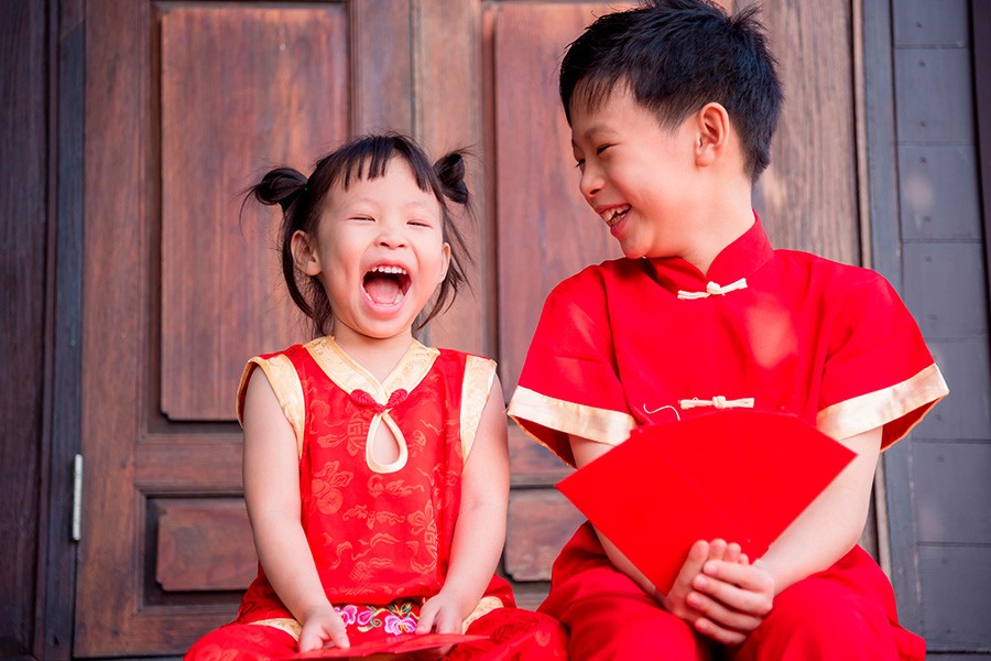 Two children in traditional Chinese clothing joyfully laughing while holding Ang Bao during Chinese New Year celebrations