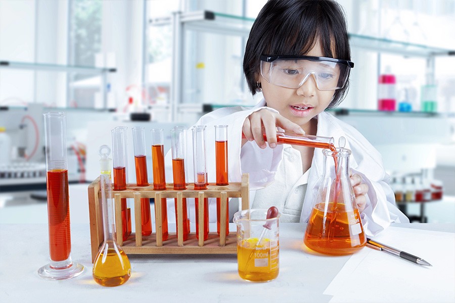 A young girl in a lab coat and glasses holds a test tube, showcasing her passion for science in extracurricular activities