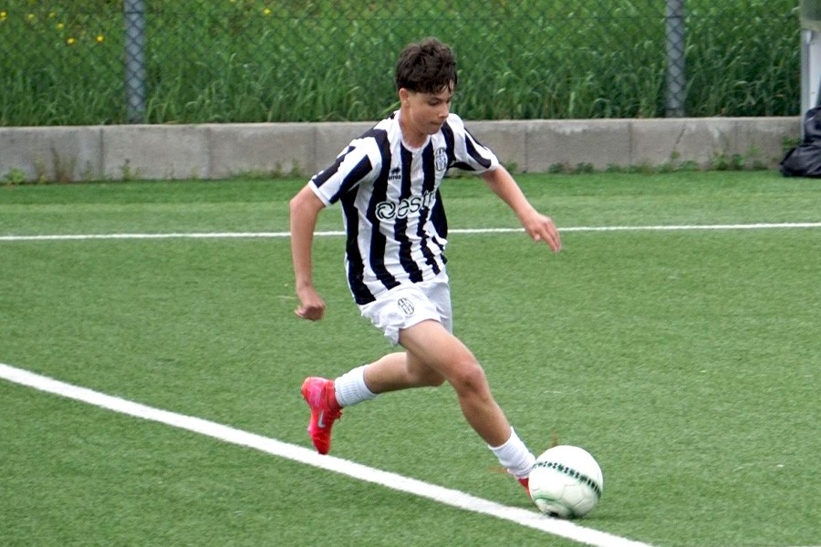 A young man in a black and white shirt runs with a soccer ball at the Siena FC Summer Camp