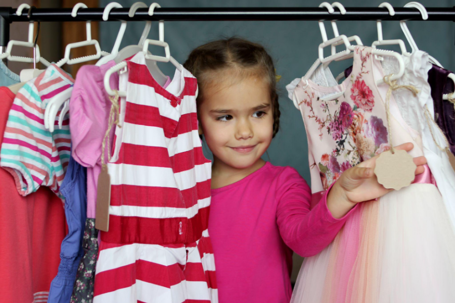 A young girl examines colorful clothes hanging on a rack in a store