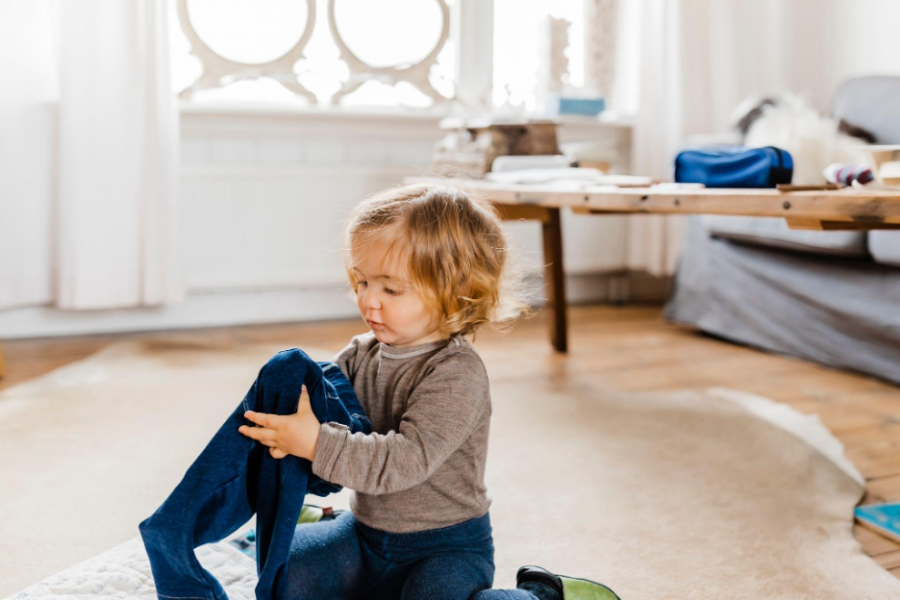 A toddler joyfully playing with a blue sock on the floor, exploring its texture and color