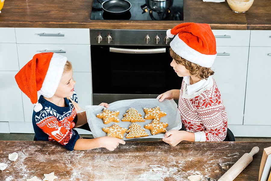 Two children wearing Christmas hats joyfully hold cookies, embodying the festive spirit of making Christmas magical for kids