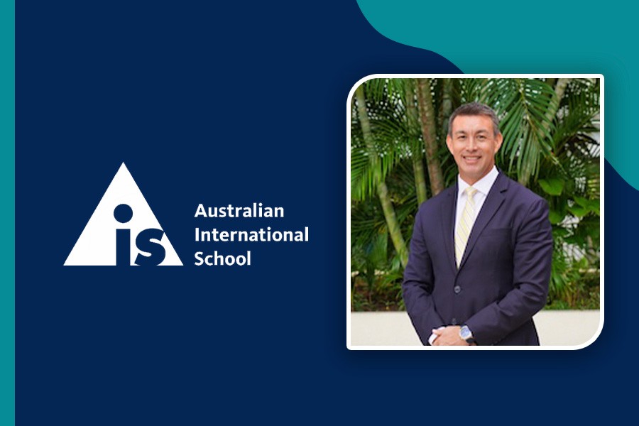 Man in a suit with a yellow tie stands smiling in front of greenery. To the left, a logo with 