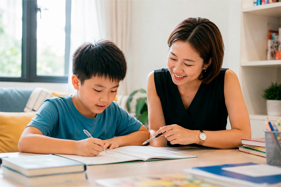 A woman assists a boy with a book, showcasing personalized tutoring at a Singapore tuition center